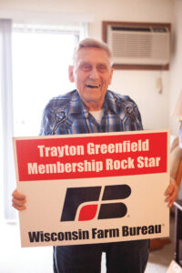 Trayton Greenfield smiles as he holds a sign that says "Trayton Greenfield Membership Rock Star"